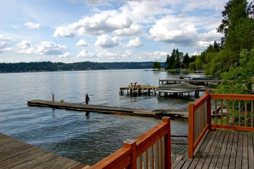 A serene lake view with docks, boats, and lush trees under a partly cloudy sky.