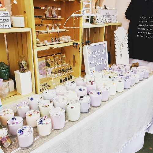 A display of various candles with floral decorations, alongside crystals and jewelry on wooden shelves.