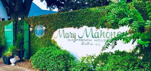Sign for Mary Mahoney's Old French House, surrounded by greenery, with a decorative gate and historical plaque.