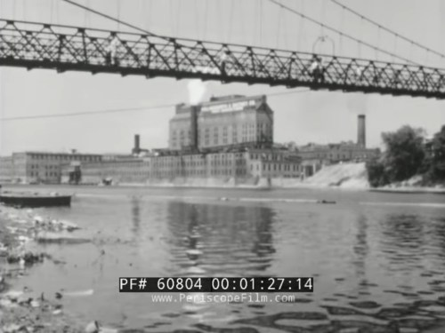 Black and white image of a bridge over a river, with a large building and shoreline visible in the background.