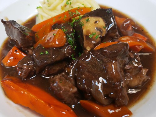 A hearty dish of beef stew with carrots, mushrooms, and mashed potatoes, garnished with parsley in a rich sauce.
