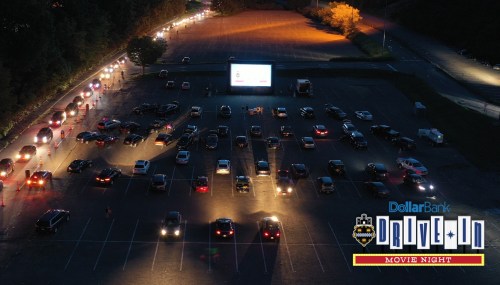 Aerial view of a drive-in movie night with cars parked in rows and a large screen displaying a film.