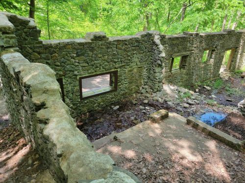 Ruins of a stone structure surrounded by lush greenery and a small stream flowing nearby.