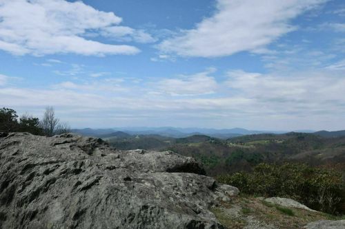 A rocky outcrop overlooks a vast landscape of rolling hills and a blue sky with scattered clouds.