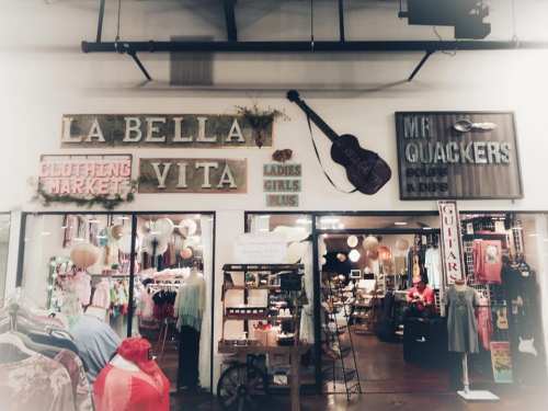 Storefront featuring "La Bella Vita Clothing Market" and "Mr. Quackers Soups & Dips," with colorful merchandise displayed.