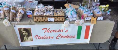 A table display of various Italian cookies for sale, featuring a sign that reads "Theresa's Italian Cookies."