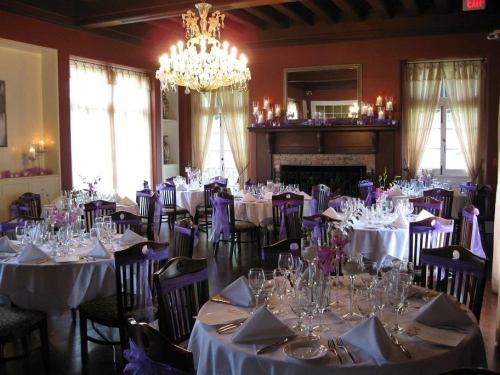 Elegant dining room set for a formal event, featuring purple accents, chandeliers, and neatly arranged tables.
