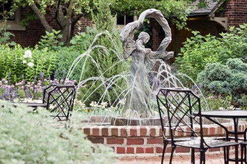 A decorative fountain featuring a statue of a woman, surrounded by lush greenery and garden seating.