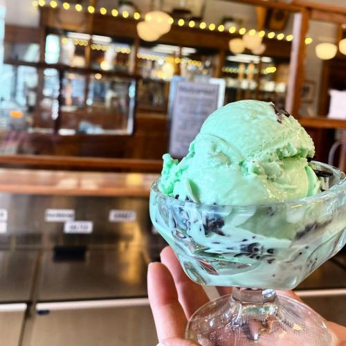 A hand holding a glass dish of mint chocolate chip ice cream in a vintage ice cream shop.