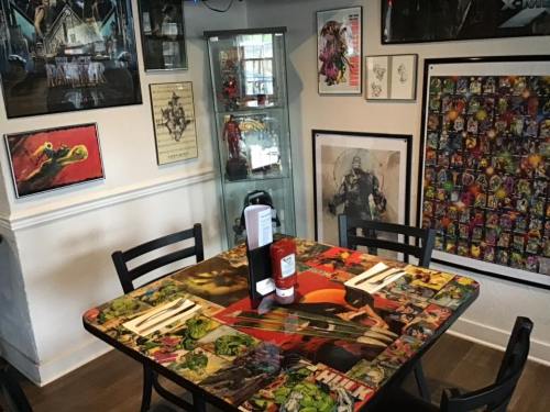 A colorful dining table with superhero artwork, surrounded by framed posters and collectibles on the walls.
