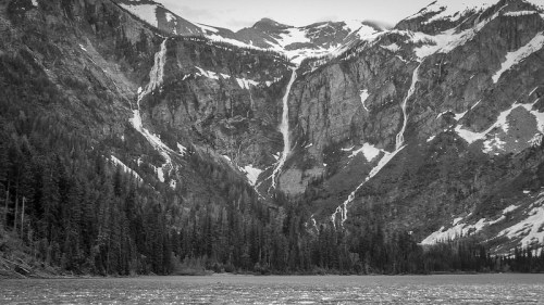Black and white image of a mountainous landscape with waterfalls cascading down rocky cliffs, surrounded by trees.