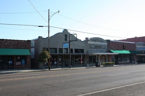 A row of historic storefronts with green awnings along a quiet street on a sunny day.