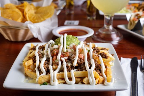 A plate of loaded fries topped with ground beef, guacamole, pico de gallo, and drizzled with sour cream.