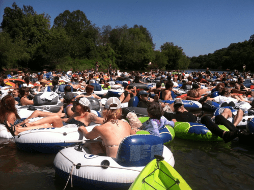 A crowded river scene with many people relaxing on inflatable tubes under a clear blue sky.