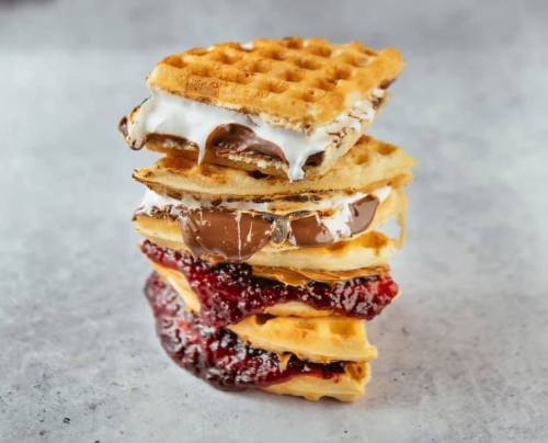 A stack of waffles layered with chocolate, marshmallow, and berry jam, creating a delicious dessert tower.