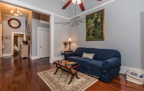 Cozy living room with a blue sofa, wooden coffee table, and a decorative rug, featuring a wall clock and artwork.