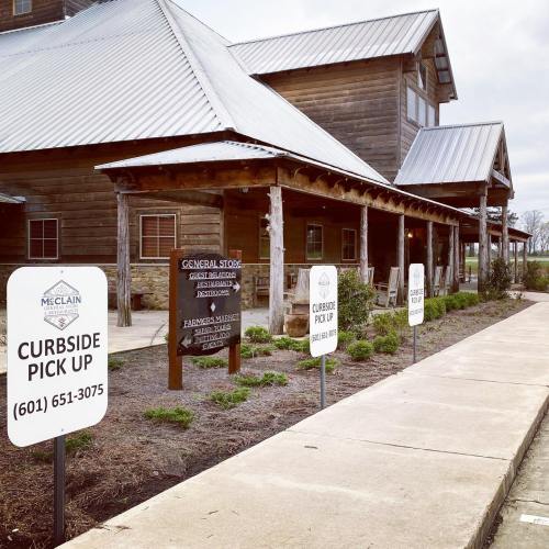 A rustic building with a metal roof, featuring signs for curbside pickup and a general store.