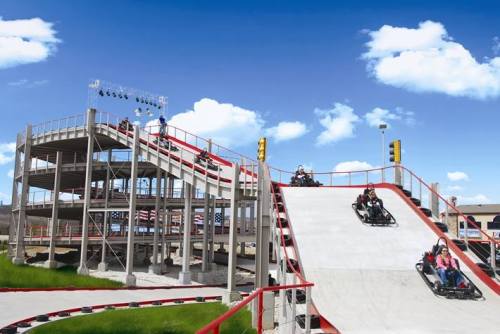 Go-karts racing down a multi-level track with a blue sky and clouds in the background.