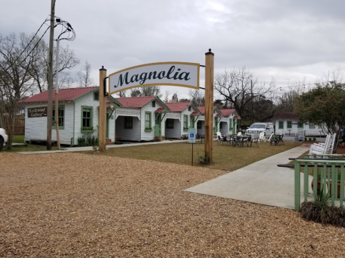 A quaint outdoor area with a sign reading "Magnolia," featuring small white buildings and gravel pathways.