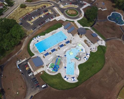 Aerial view of a large outdoor swimming pool complex with slides, lounge areas, and surrounding green space.