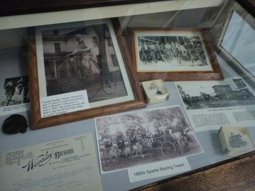 Display case featuring historical photos and memorabilia of the 1890s Sparta Racing Team and early bicycles.