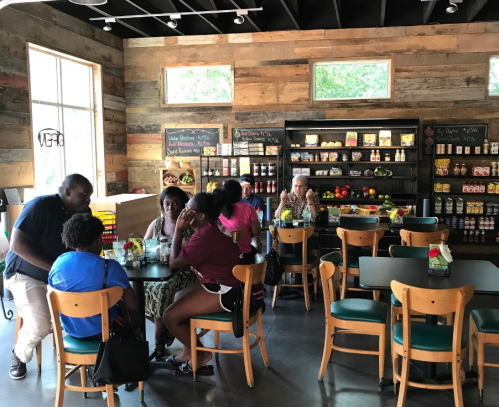 A cozy café interior with wooden walls, featuring a group of people at tables and shelves stocked with food items.