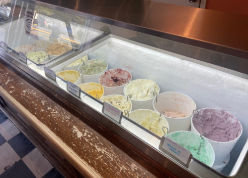 A display of various ice cream flavors in tubs, arranged in a glass case with labels in front of each tub.
