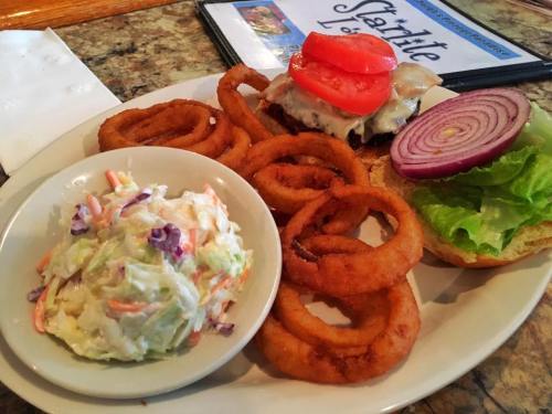 A plate with a burger topped with tomato, onion, lettuce, onion rings, and a side of coleslaw.