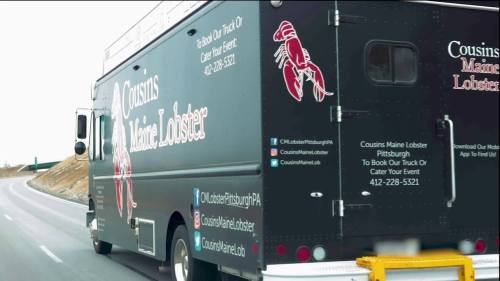 A food truck with "Cousins Maine Lobster" branding driving on a highway, promoting catering services in Pittsburgh.