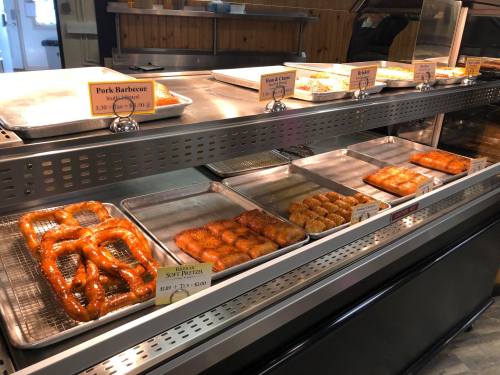 A display of various food items in trays, including pretzels and barbecue, with price tags visible.