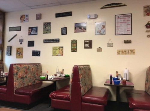 A cozy diner interior with floral booths and a wall decorated with various vintage signs and menus.