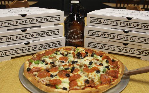 A delicious pepperoni pizza with olives and green peppers, surrounded by pizza boxes and a growler of beer.