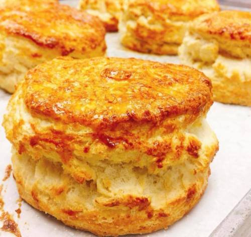 Golden, flaky biscuits stacked on a baking sheet, showcasing a crispy top and soft, airy interior.