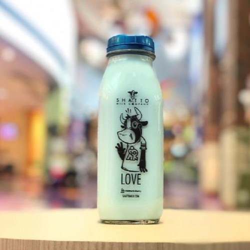A glass bottle of light blue milk with a cartoon cow and the word "LOVE" printed on it, set against a blurred background.
