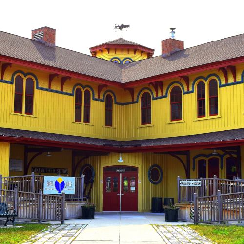 A bright yellow building with red accents, featuring a central tower and signs for a museum and train station.
