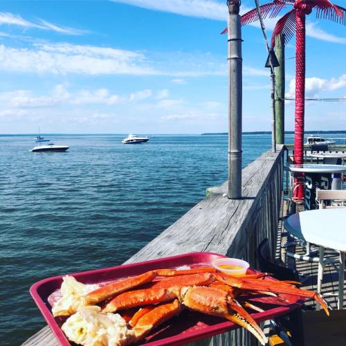A tray of crab legs and dipping sauce on a dock overlooking a calm waterway with boats in the distance.
