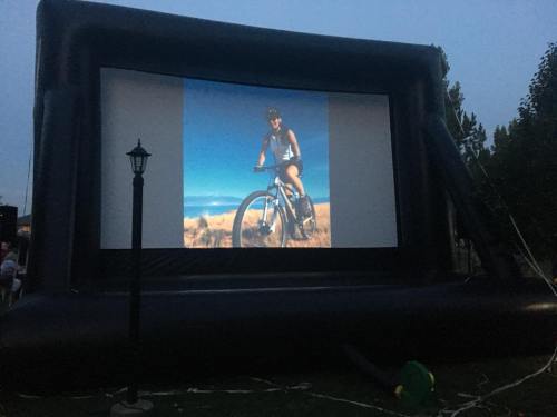 A large inflatable screen displays a photo of a person riding a bicycle in a scenic outdoor setting.