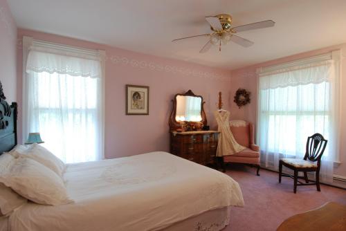 Cozy bedroom with a pink color scheme, featuring a bed, vintage furniture, and soft natural light from large windows.