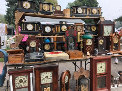 A display of various vintage clocks on a wooden shelf at an outdoor market.
