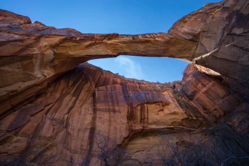 A stunning view of a natural rock arch against a clear blue sky, framed by towering red rock cliffs.