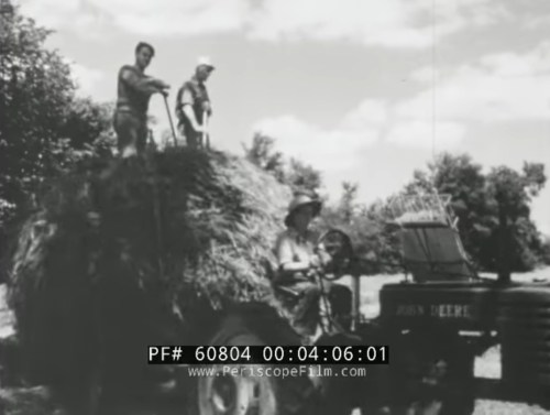 Black and white image of three men on a tractor loaded with hay, working on a farm under a sunny sky.