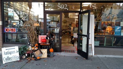 A storefront with an open door, displaying antiques and collectibles, decorated with pumpkins and fall decor.