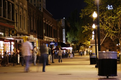 A lively street at night with people walking, outdoor seating, and illuminated buildings.