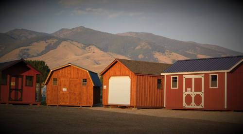 A row of wooden storage sheds in various styles, set against a backdrop of mountains and a clear sky.