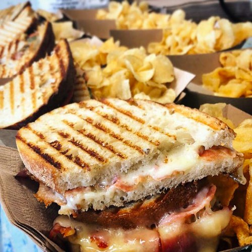 A grilled sandwich with melted cheese and ham, served with a side of crispy potato chips.