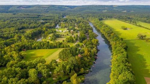 Aerial view of a lush green landscape with a winding river, fields, and scattered homes surrounded by trees.