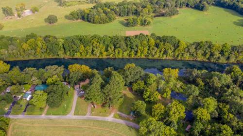 Aerial view of a river bordered by lush trees, with fields and houses nearby in a rural landscape.