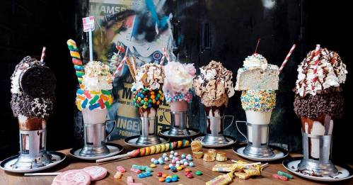 A colorful display of extravagant milkshakes topped with whipped cream, candies, and various treats on a table.