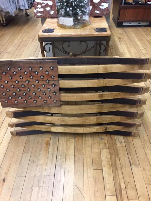 A wooden American flag art piece made from slats, featuring stars and stripes, displayed on a wooden floor.