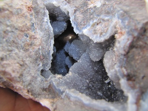 Close-up of a rock with a hollow cavity filled with small, sparkling gray crystals.